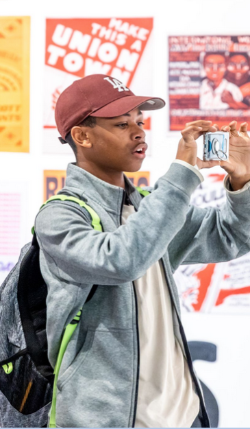 male presenting black youth taking a photo of art on white walls